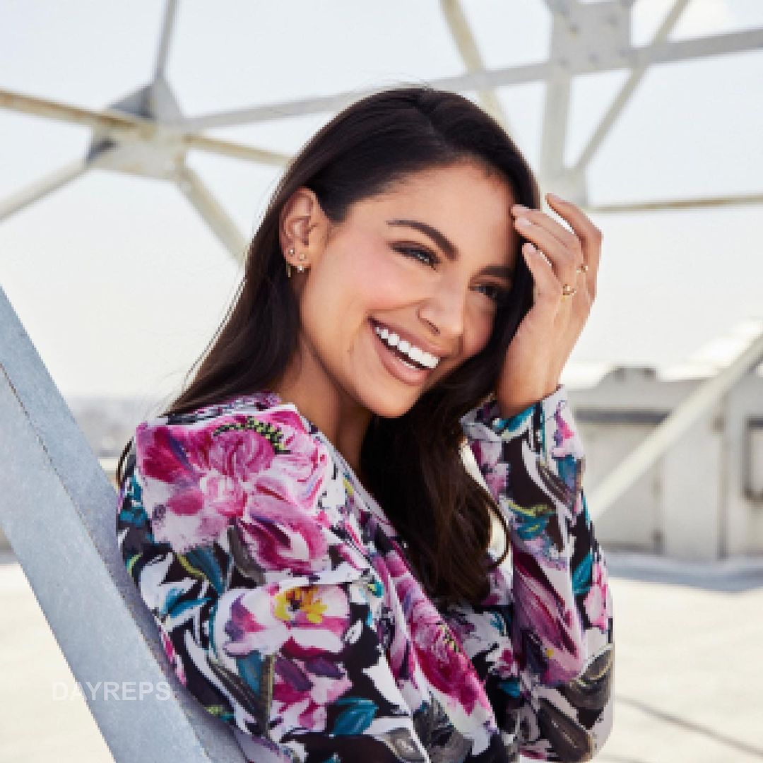 Portrait of a smiling woman with floral blouse outdoors. She is posing in front of an urban structure with the sky in the background.