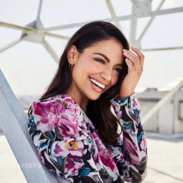 Portrait of a smiling woman with floral blouse outdoors. She is posing in front of an urban structure with the sky in the background.