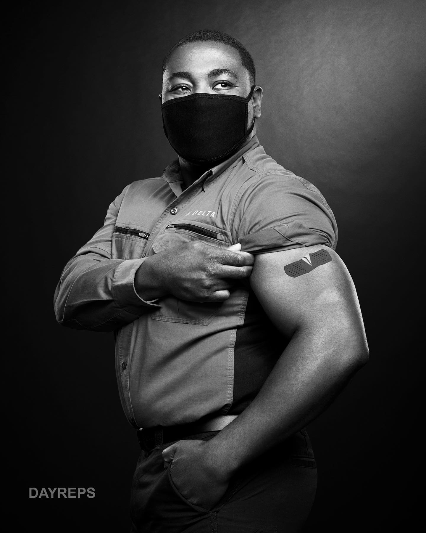 Portrait of a man wearing a face mask and showing his arm with a vaccine bandage against a dark background in a studio setting.