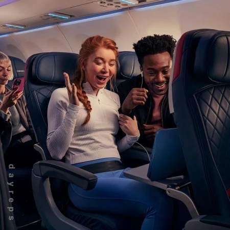 Three people on an airplane are watching a laptop. Two people are looking at the screen with smiling expressions.