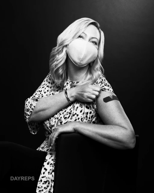Monochrome shot of an adult woman with blonde hair wearing a mask and a bandage on her arm after receiving the vaccine.