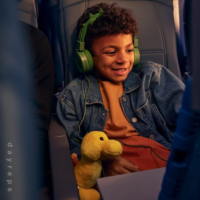 Young boy smiles wearing green headphones on an airplane, holding a plush duck toy, creating a heartwarming scene of childhood travel.