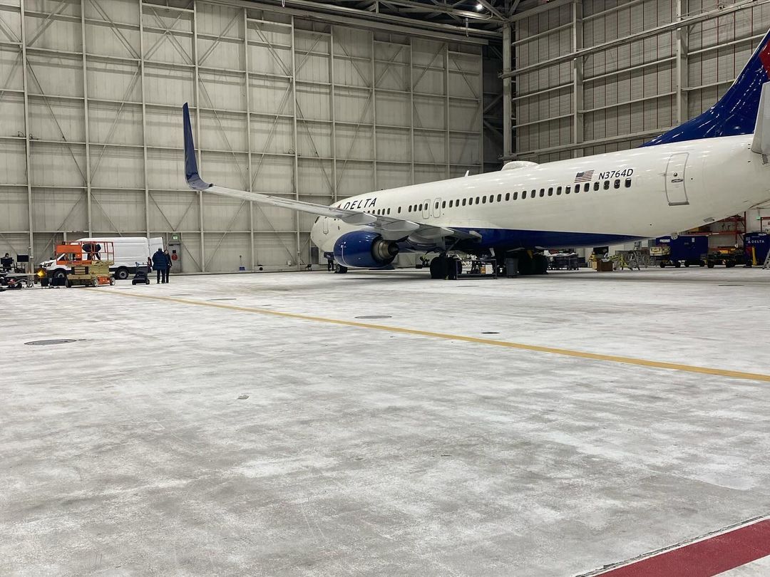 Aircraft in a hangar with maintenance crew and vehicles visible in the background, capturing the scale of aviation engineering.