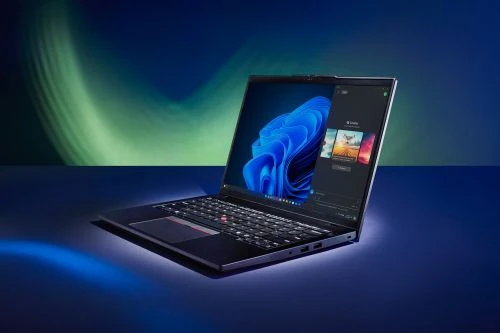 Modern laptop computer opened on a dark blue surface with a glowing abstract blue screen wallpaper and soft green and blue background lighting.