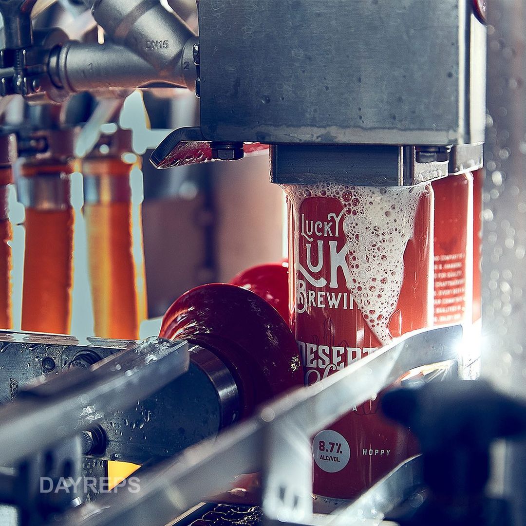 Cans of Lucky U Brewing beer moving on an automated production line, being filled with beer and foam in a brewery setting.