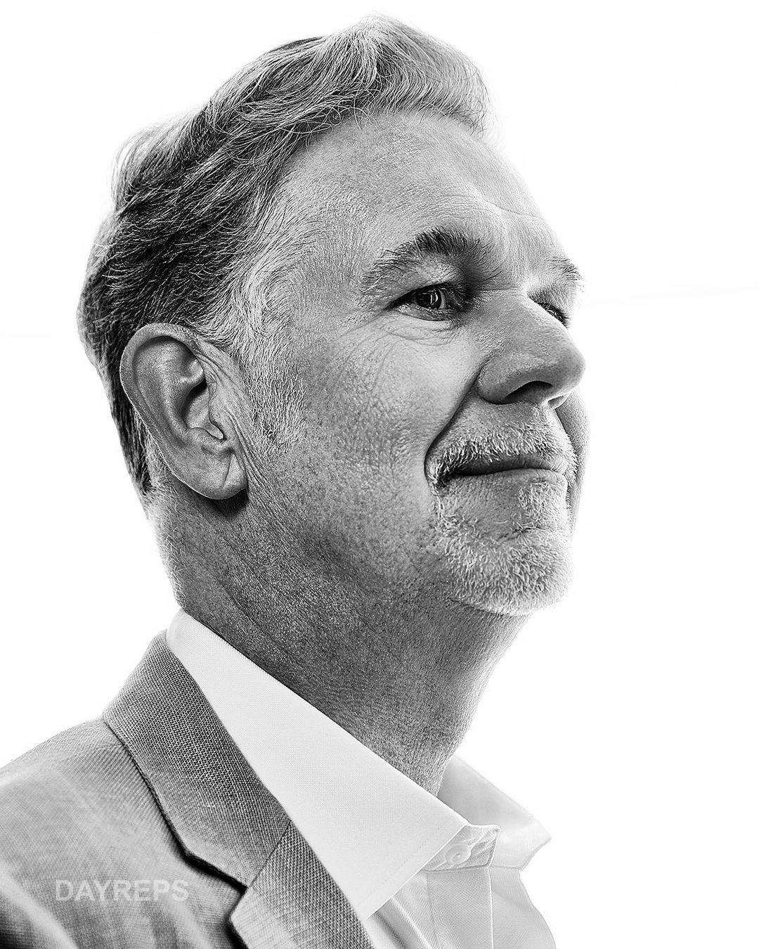 Black and white portrait of a mature man in a suit, looking upward against a bright background, captured in a close-up, low-angle shot.
