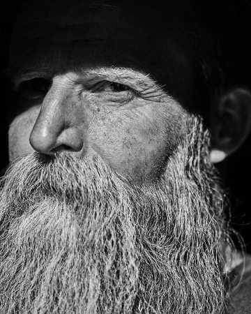 Close-up black and white portrait of an elderly man with a long textured beard and serious expression by Christopher Patey