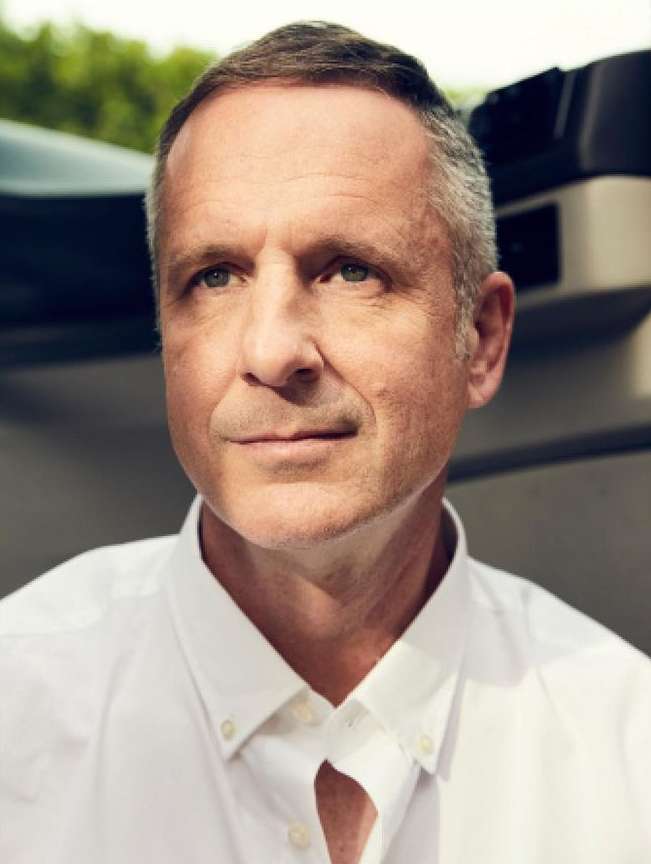 Portrait of a middle-aged Caucasian man with short hair, wearing a button-down shirt, posing in front of a car.