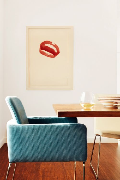 Interior view of a mid-century modern home with a blue chair, hardwood floor, and a framed lips art print on a white wall.