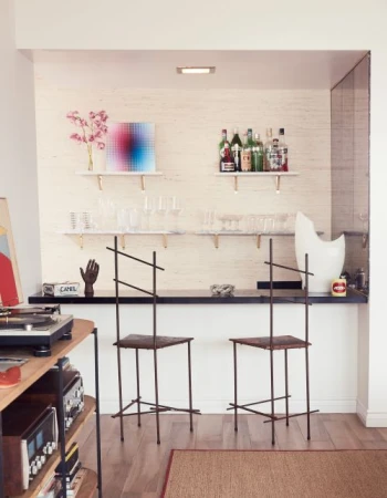 Interior shot of two unique chairs at a sleek, modern home bar with alcohol bottles and decorative objects on floating shelves.