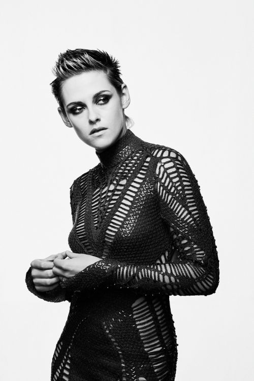 Black-and-white portrait of a fair-skinned adult woman with dark eye makeup and a short, spiky haircut, wearing a textured black dress.
