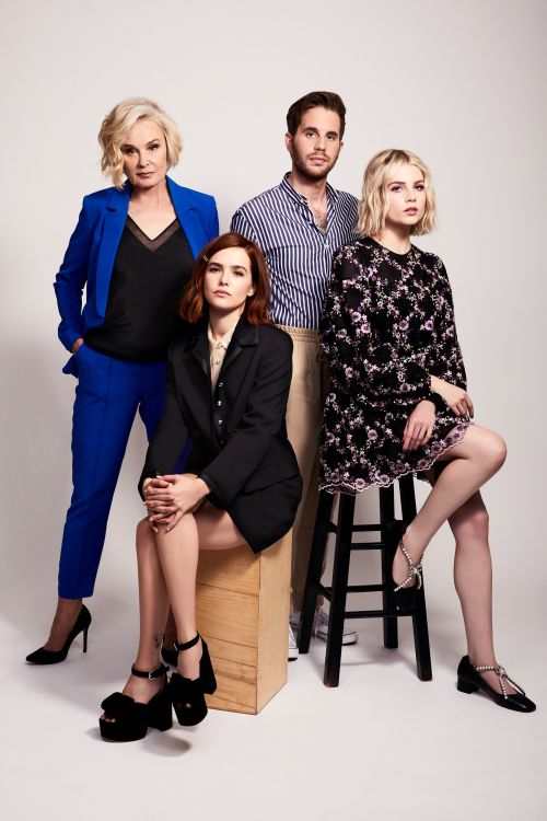 Four adults: two women standing, one seated, and one man standing in a studio setting, modelling fashion apparel and shoes.