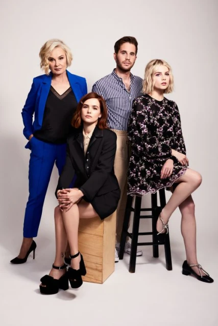Four adults: two women standing, one seated, and one man standing in a studio setting, modelling fashion apparel and shoes.