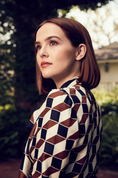 Portrait of a beautiful woman with auburn hair wearing a patterned blouse, gazing thoughtfully in an outdoor setting with foliage background.