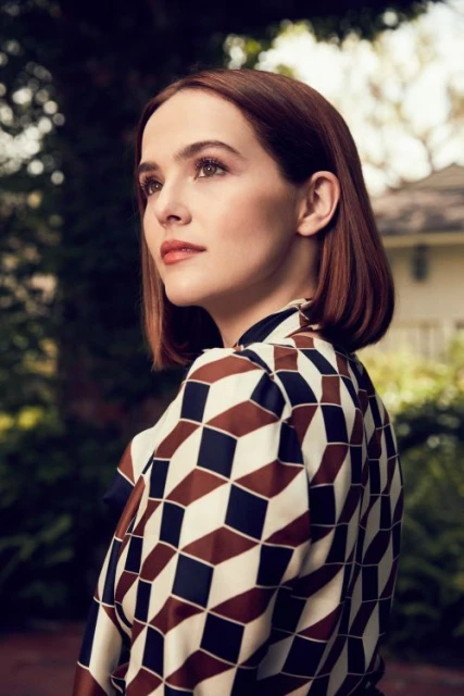 Portrait of a beautiful woman with auburn hair wearing a patterned blouse, gazing thoughtfully in an outdoor setting with foliage background.