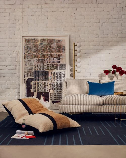 Interior view of a living room with a floor pillow, a graphic art print, a modern couch, and a geometric patterned blue rug.