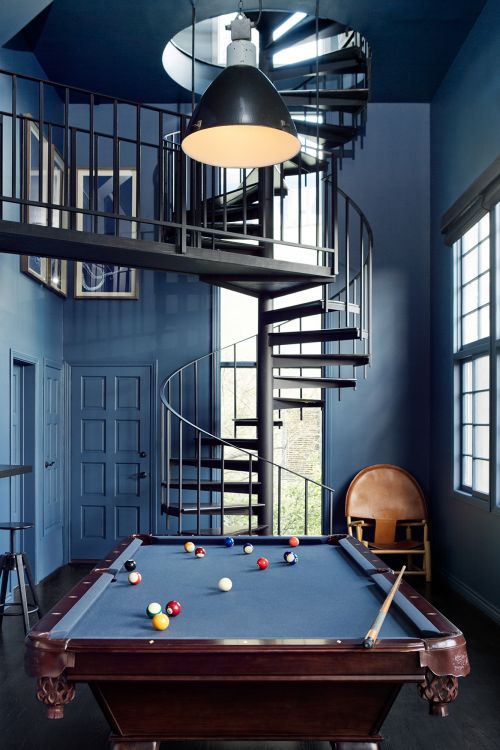 Indoor game room featuring a pool table with pool balls, a spiral staircase, and overhead lighting in a room with blue walls.