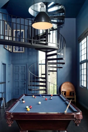 Indoor game room featuring a pool table with pool balls, a spiral staircase, and overhead lighting in a room with blue walls.