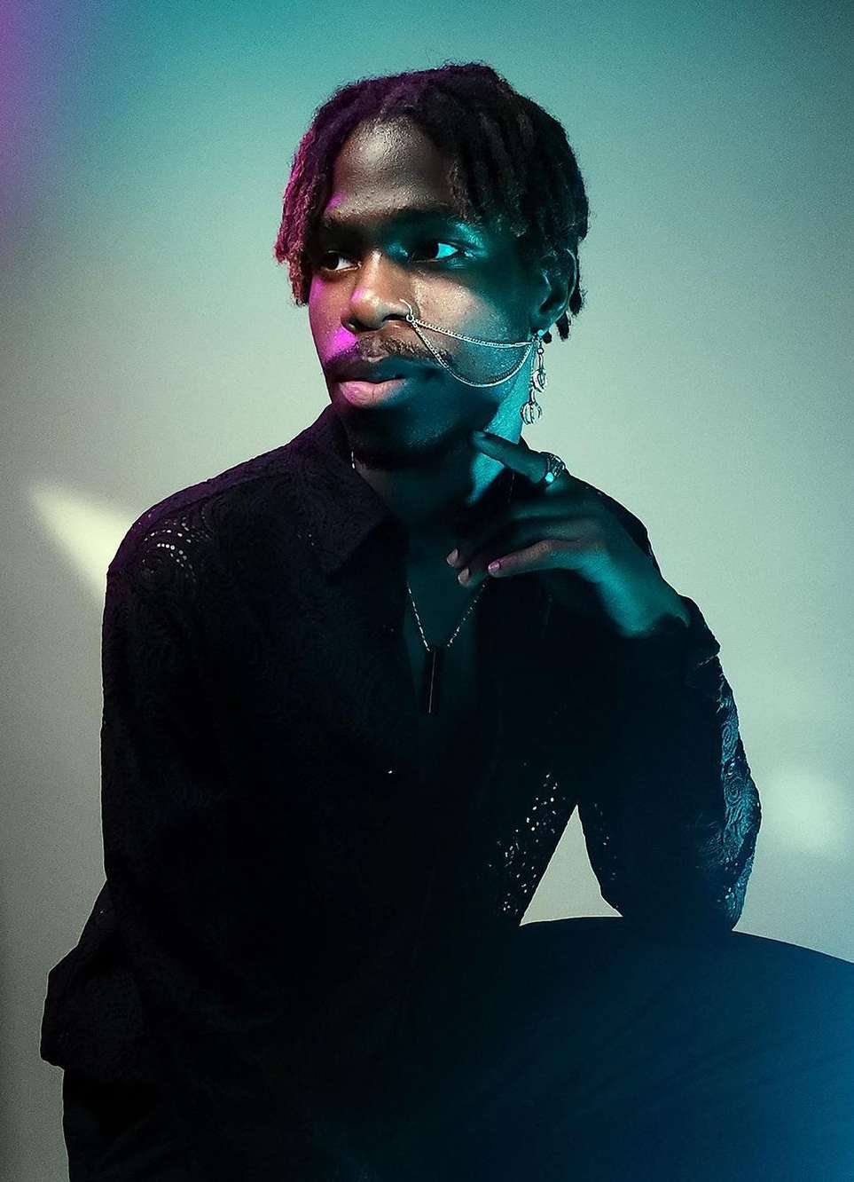 Portrait of Black adult male with dreadlocks in black lace shirt. Man is wearing jewelry and posing in a studio with blue lighting.