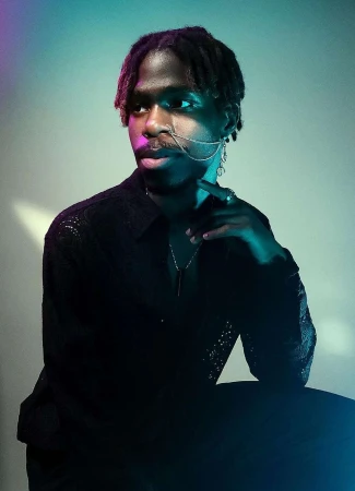 Portrait of Black adult male with dreadlocks in black lace shirt. Man is wearing jewelry and posing in a studio with blue lighting.