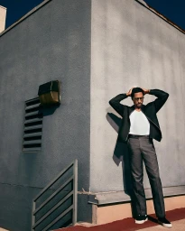 Man in dark jacket and grey trousers standing against a textured grey building exterior in Los Angeles by Christopher Patey.