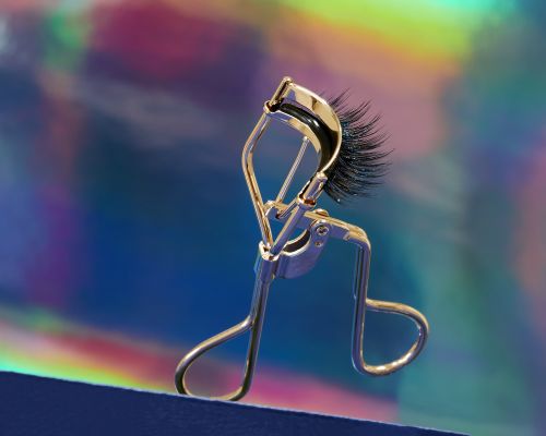 Close-up of an eyelash curler with false eyelashes against a colorful background. Beauty product shot for makeup application.
