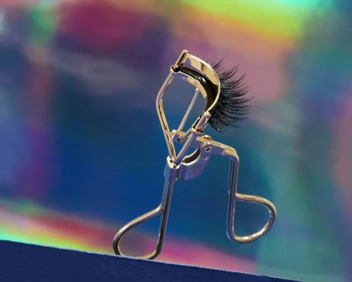 Close-up of an eyelash curler with false eyelashes against a colorful background. Beauty product shot for makeup application.
