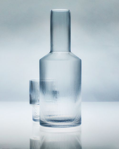 Glass carafe and matching glass in a studio shot against a graduated light blue background, showcasing design and clarity.
