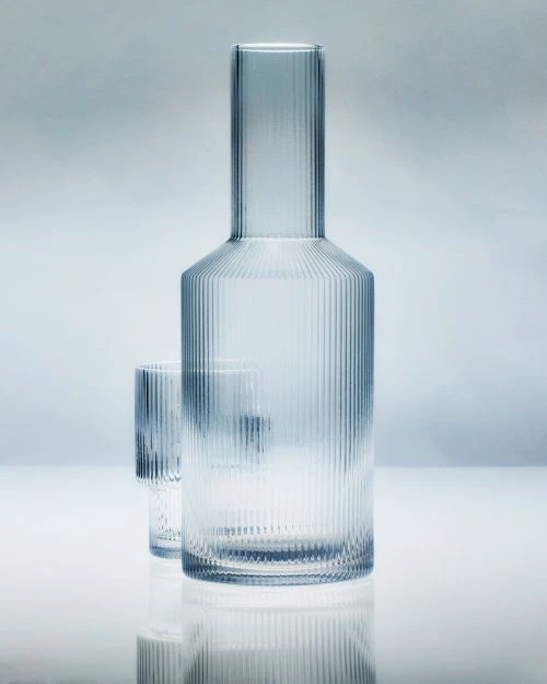 Glass carafe and matching glass in a studio shot against a graduated light blue background, showcasing design and clarity.