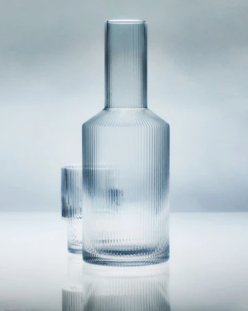Glass carafe and matching glass in a studio shot against a graduated light blue background, showcasing design and clarity.