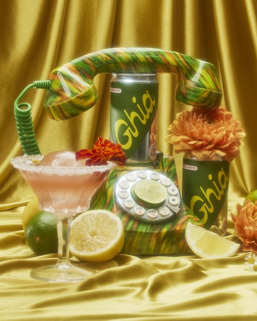 Retro aesthetic still life with Ghia cans, vibrant lemons, and a patterned rotary phone against a textured gold backdrop.