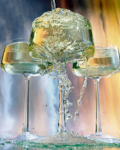Champagne pours into glasses creating a splash effect; celebratory toast with sparkling beverage in elegant glassware against a blurred backdrop.