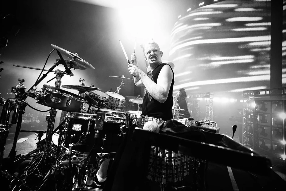 Monochrome shot of a drummer playing on stage with drum set, illuminated by bright stage lights creating a high-energy performance atmosphere.