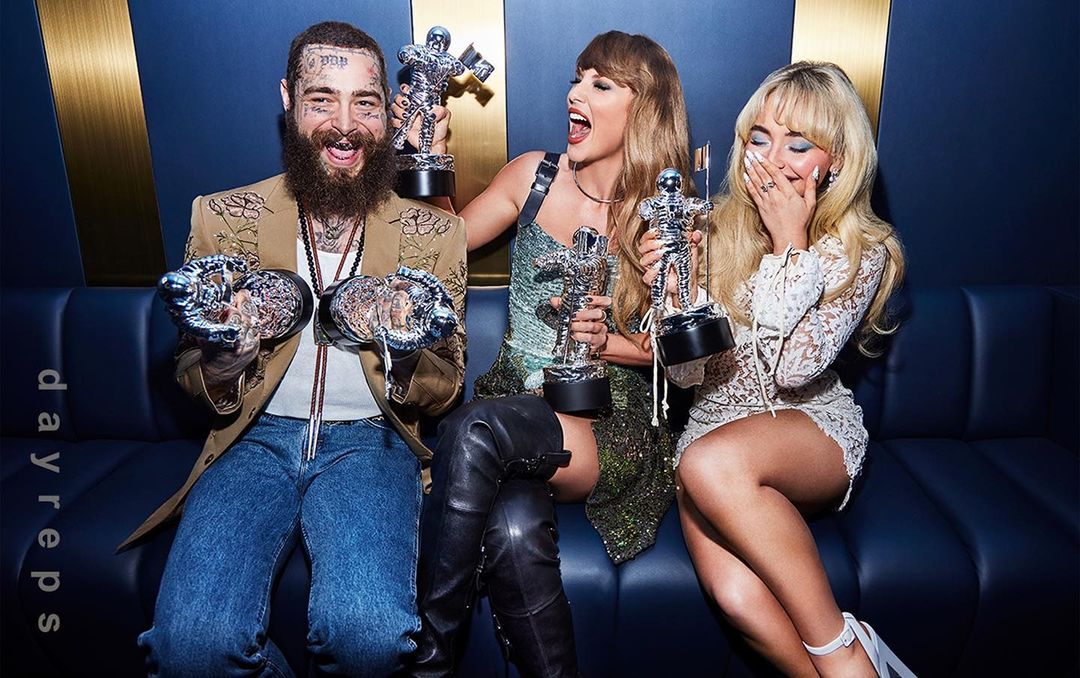 Post Malone, Taylor Swift, and Sabrina Carpenter seated on a blue couch, holding MTV Video Music Awards Moonman trophies.