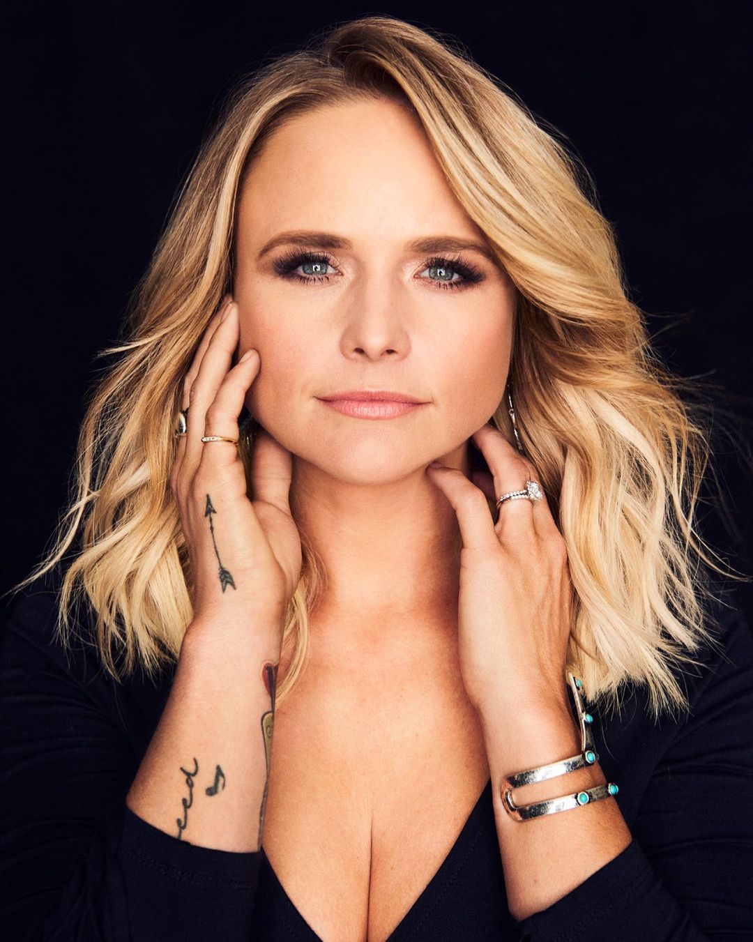 Close-up studio portrait of Miranda Lambert, a blonde woman with fair skin, wearing a black top and turquoise jewelry, looking at camera.