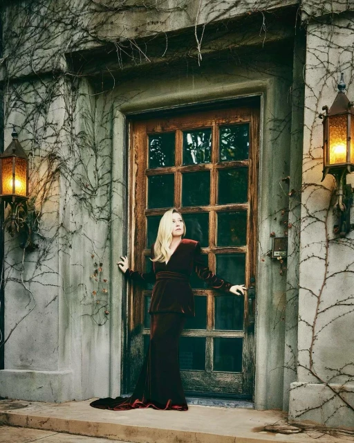 Woman in a velvet gown poses in front of an old wooden door with stone archway and vines growing on the exterior of the building.