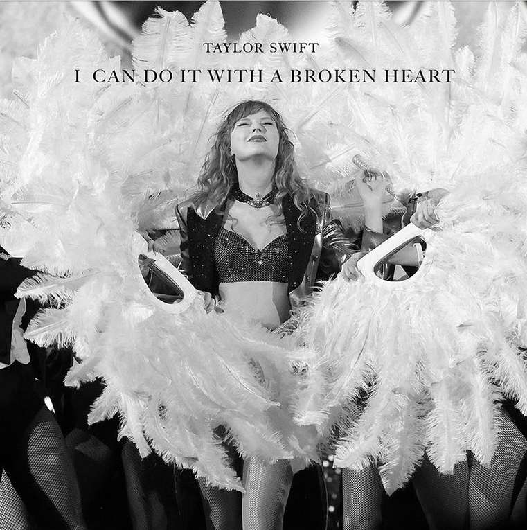 Black and white portrait of Taylor Swift in concert attire with feathered fans, with stage lighting and multiple dancers in the background.