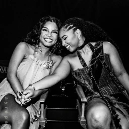 Two smiling Black women holding hands in close-up portrait by John Shearer, captured in monochrome.