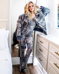 Blonde woman wearing matching patterned jacket and pants leaning against a white dresser in a room