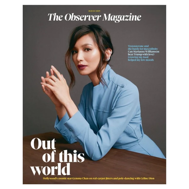 Magazine cover featuring Gemma Chan in a blue outfit, resting her hands, set against a grey backdrop and a wooden table surface.