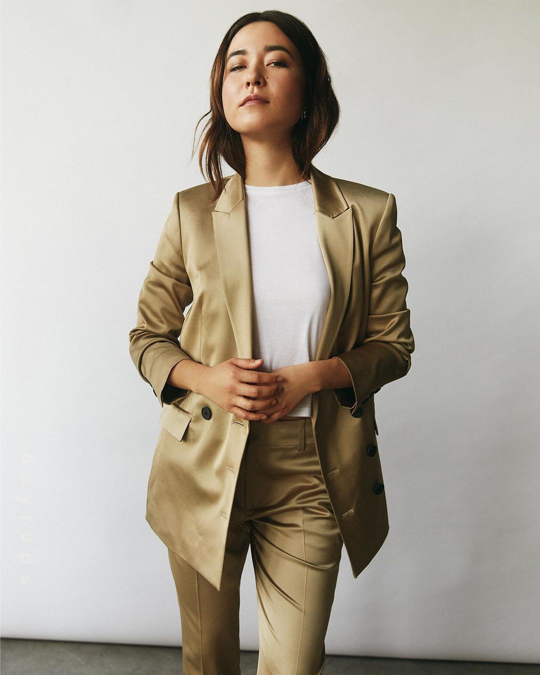 Woman wearing a golden satin suit jacket and trousers over a white t-shirt against a white background