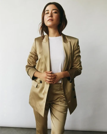 Woman wearing a golden satin suit jacket and trousers over a white t-shirt against a white background