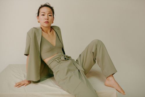 Elegant woman in a green, two-piece suit poses on a cream-colored surface against a neutral backdrop in a fashion editorial setting.