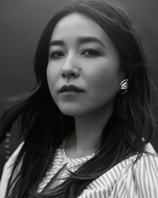 Monochrome portrait of an adult woman with long dark hair, wearing a vertically striped shirt and large geometric earring, against a dark background.