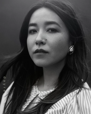 Monochrome portrait of an adult woman with long dark hair, wearing a vertically striped shirt and large geometric earring, against a dark background.