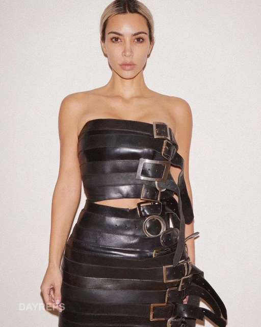 Adult female wearing a black strapless top and skirt with silver buckle detailing against a plain white background in a studio shot.