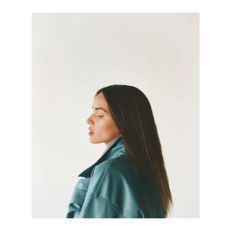 Profile portrait of a woman with long dark hair wearing a teal jacket against a plain white background