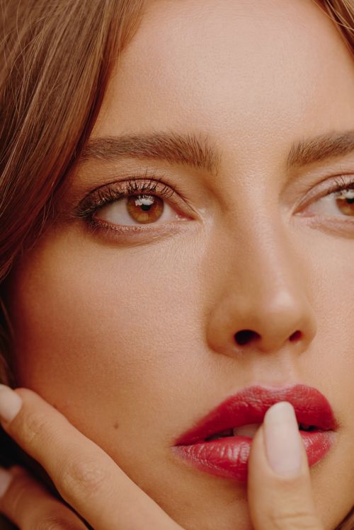 Close-up portrait of a woman with brown eyes, red lips, and manicured nails, with focus on beauty and cosmetics in a studio setting.