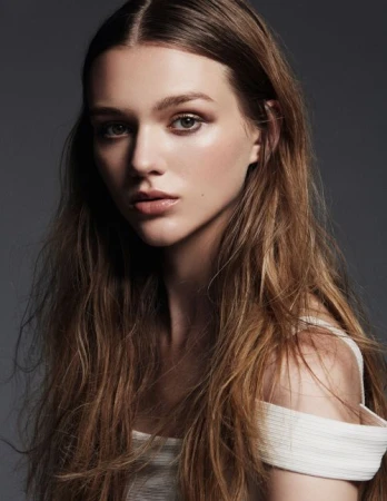 Portrait of a woman with long brown hair wearing a white top against a dark grey seamless studio background.
