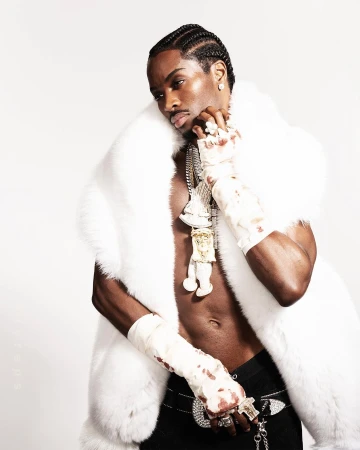 Black man wearing a white fur vest and heavy diamond chains posing against a white background